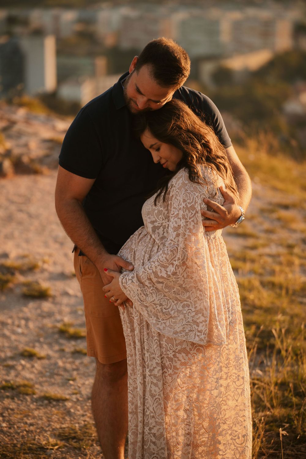 Intimate maternity portrait with couple embracing on rocky terrain during golden hour.