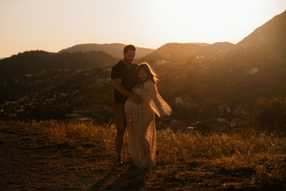 Silhouetted couple embraces during sunset maternity shoot on mountain trail.