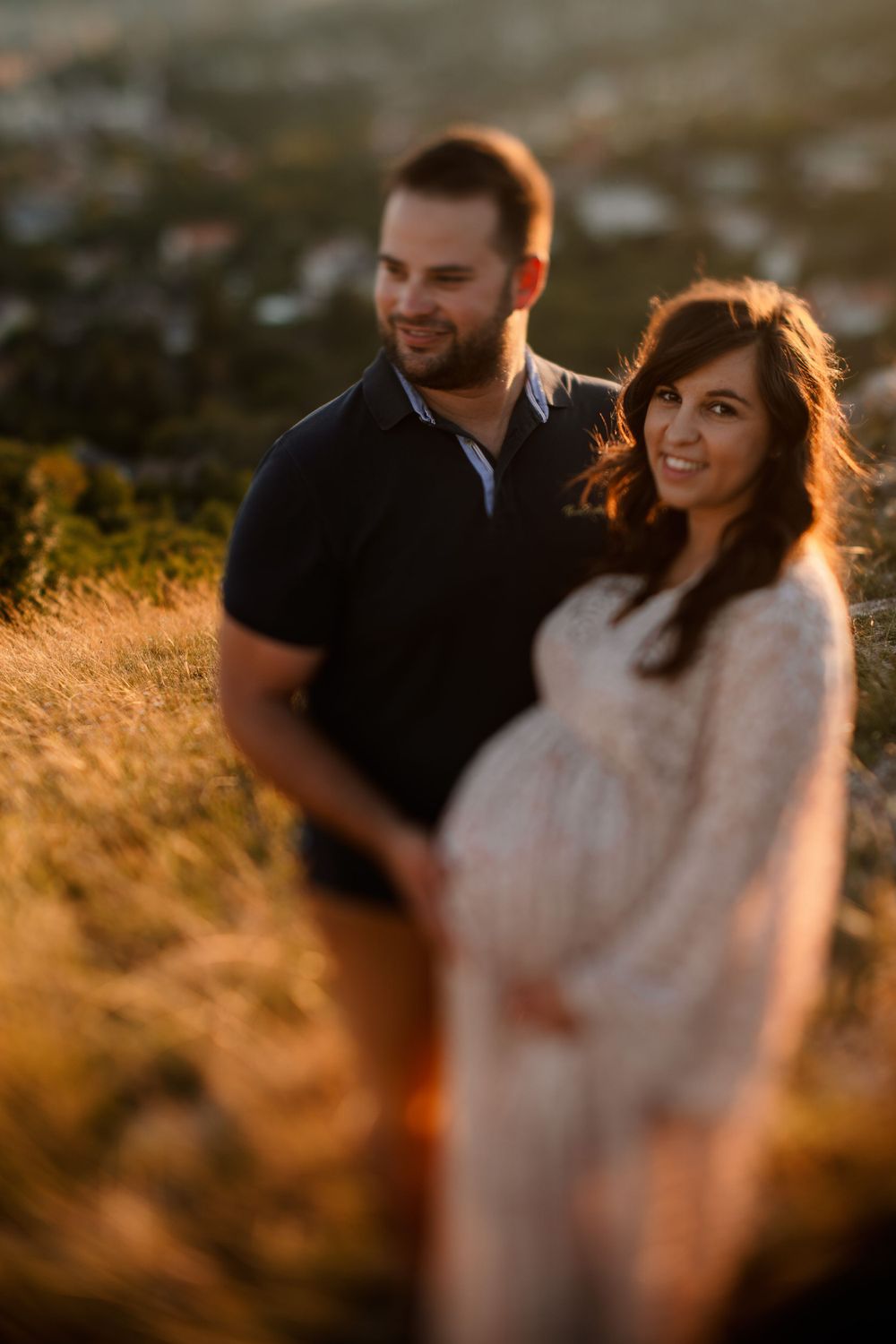 A couple poses during golden hour on a hilltop for their maternity photography session.