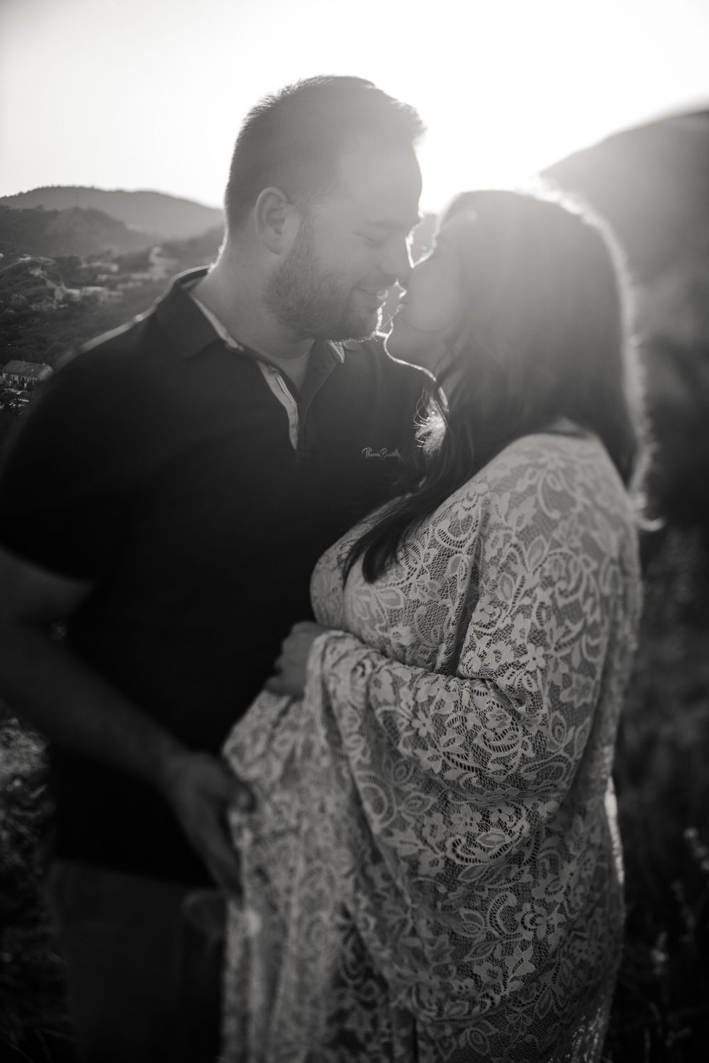 A backlit couple shares an intimate moment during their maternity photo session in nature.