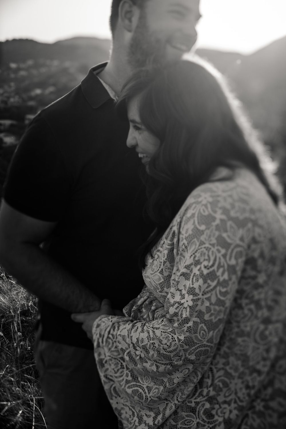 A couple shares a tender moment during their black and white maternity photo shoot on a hillside.
