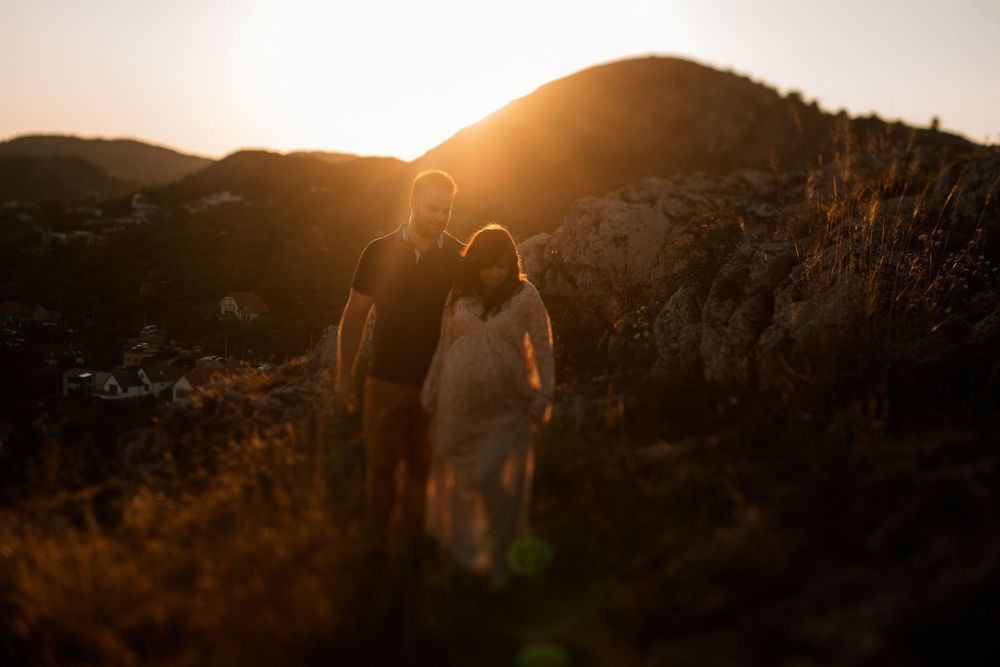 Couple standing together on hillside during golden hour sunset with mountains in background.