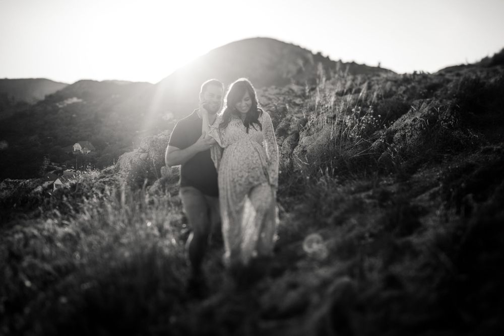 Silhouetted couple embracing on hilltop with sun rays creating dramatic backlight.
