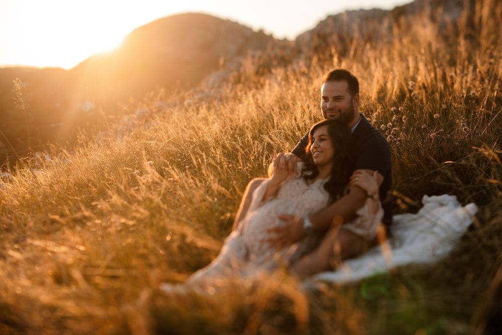 Romantic couple relaxing on blanket in tall grass during sunset on mountainside.