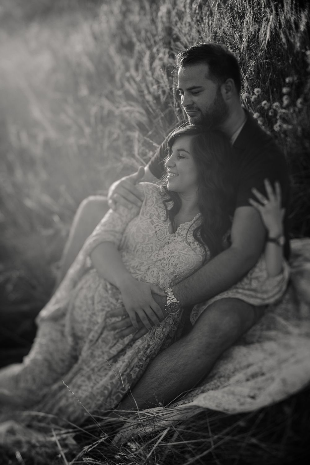 Tender black and white portrait of couple embracing on hillside in natural setting.