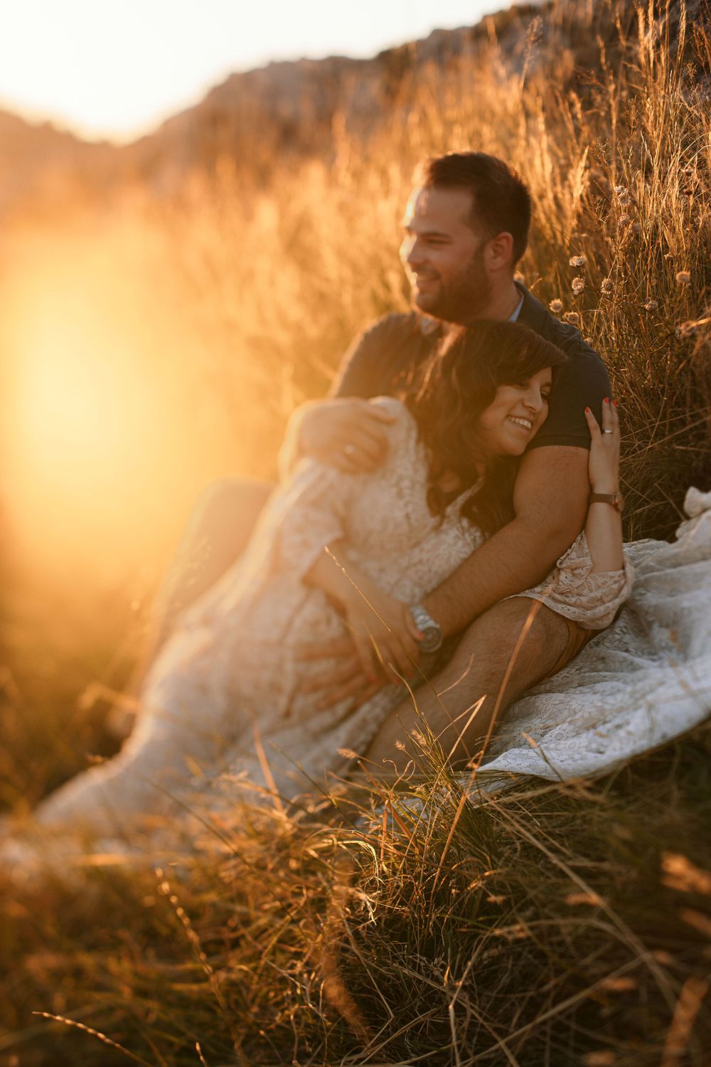 Couple sharing intimate moment on hillside during golden hour sunset.
