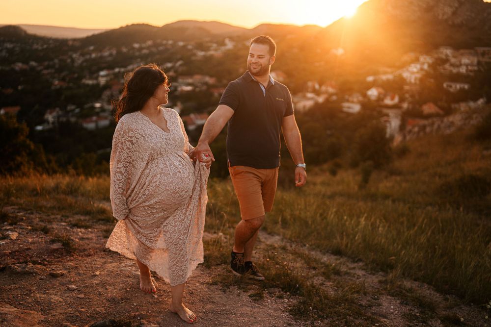 Couple walking hand in hand on mountain path during warm sunset light.