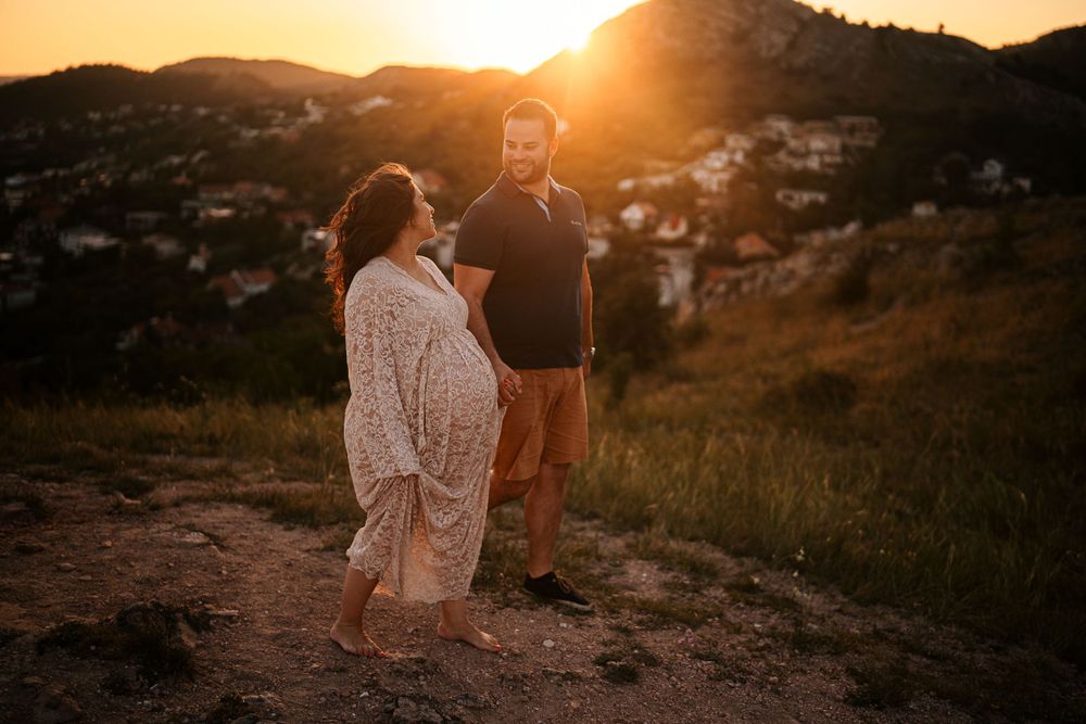 Couple standing on mountain trail overlooking city during vibrant sunset.