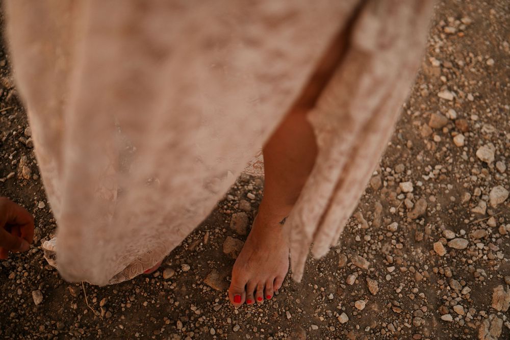 Bare feet on rocky ground peek out from beneath a blush-colored dress.