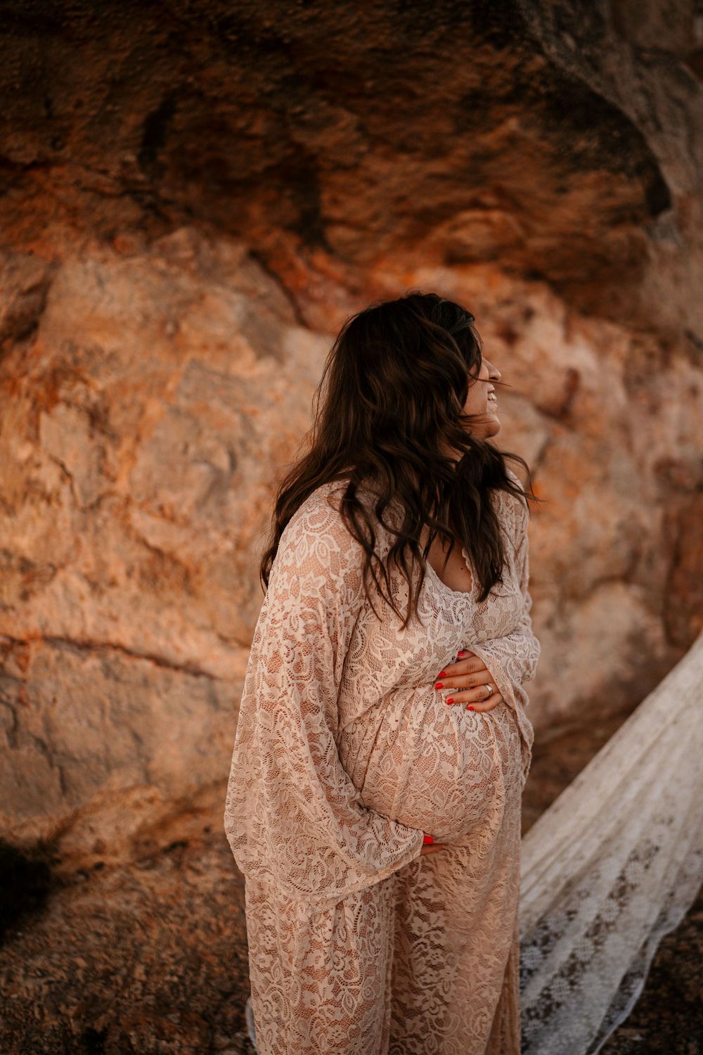 Maternity photo featuring a lace dress against warm-toned rocky cave walls.