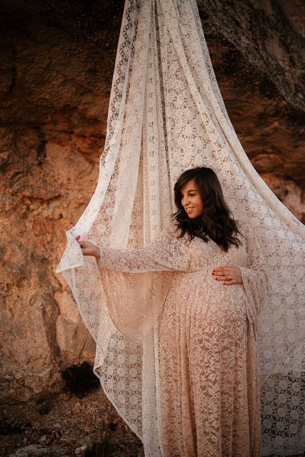 Ethereal maternity portrait with flowing lace fabric draped in a cave setting.