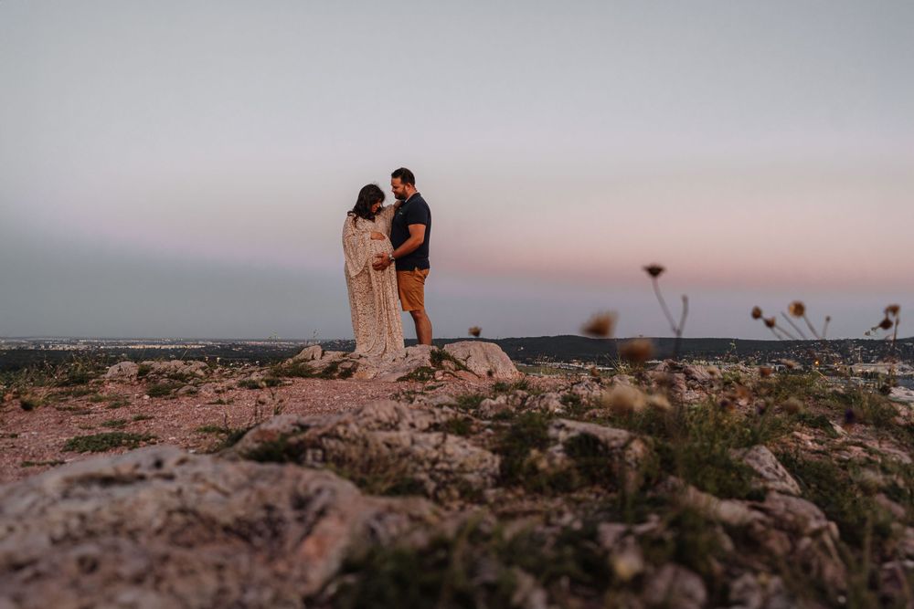 A romantic couple pose together on a rocky cliff overlooking a scenic desert landscape at dusk.