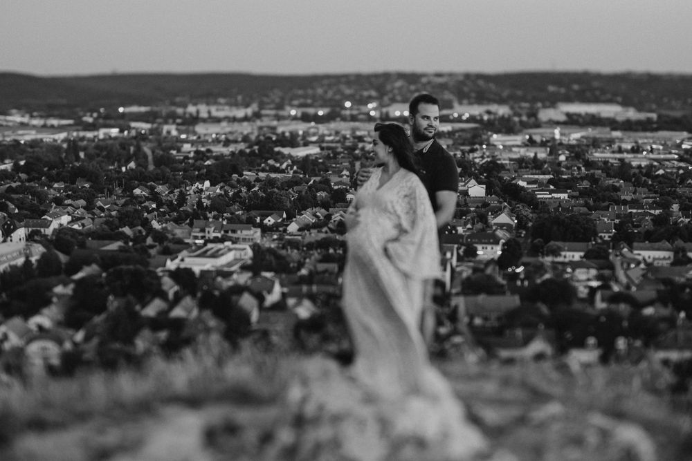 A black and white cityscape photo of a couple embracing on a hilltop overlook.