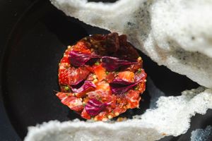 Close-up of a colorful circular dish with red and purple ingredients against black background.