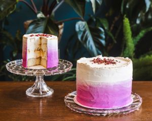Two pink ombre cakes with white frosting displayed on crystal cake stands against a dark background.