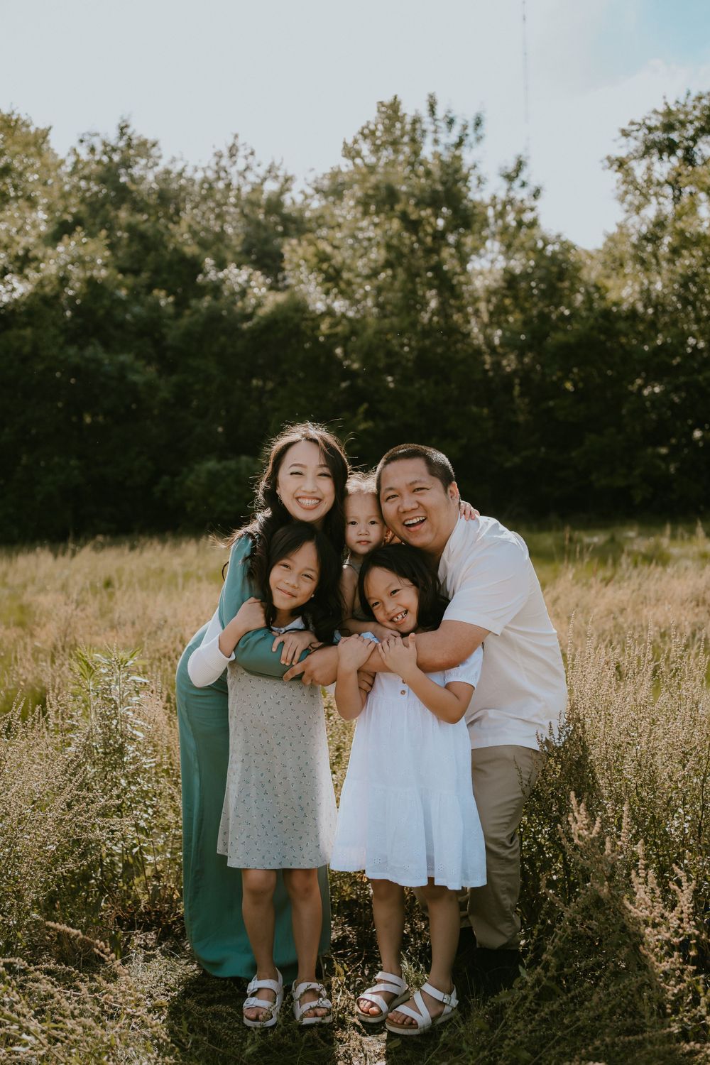 A happy family of five poses together in a sunlit meadow during golden hour.