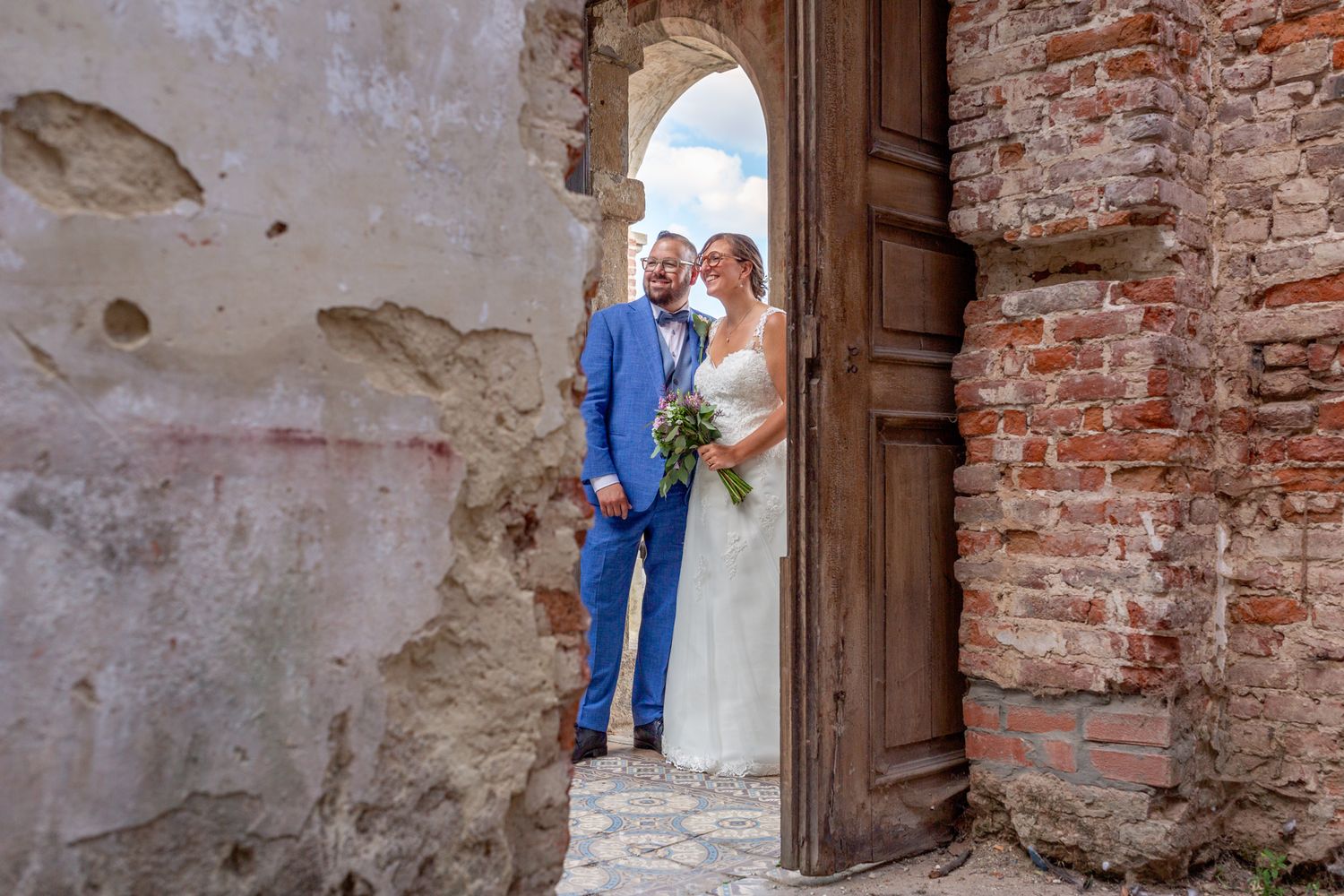 A wedding couple poses in a rustic brick doorway of an old stone building.