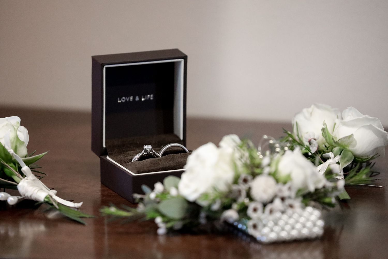 Wedding rings in black box with white roses and pearl details.