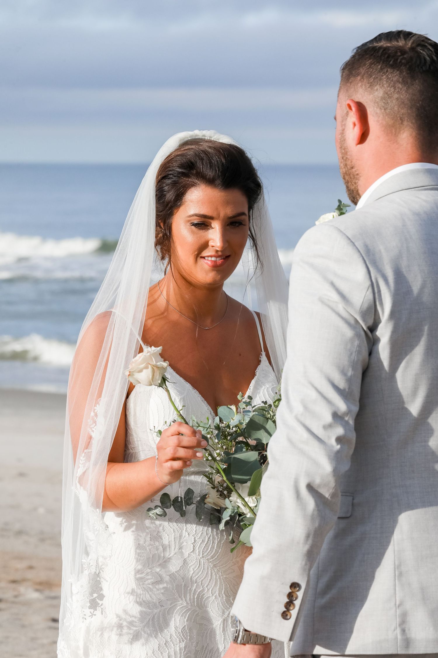 A bride and groom share an intimate moment on a beach with crashing waves in the background.