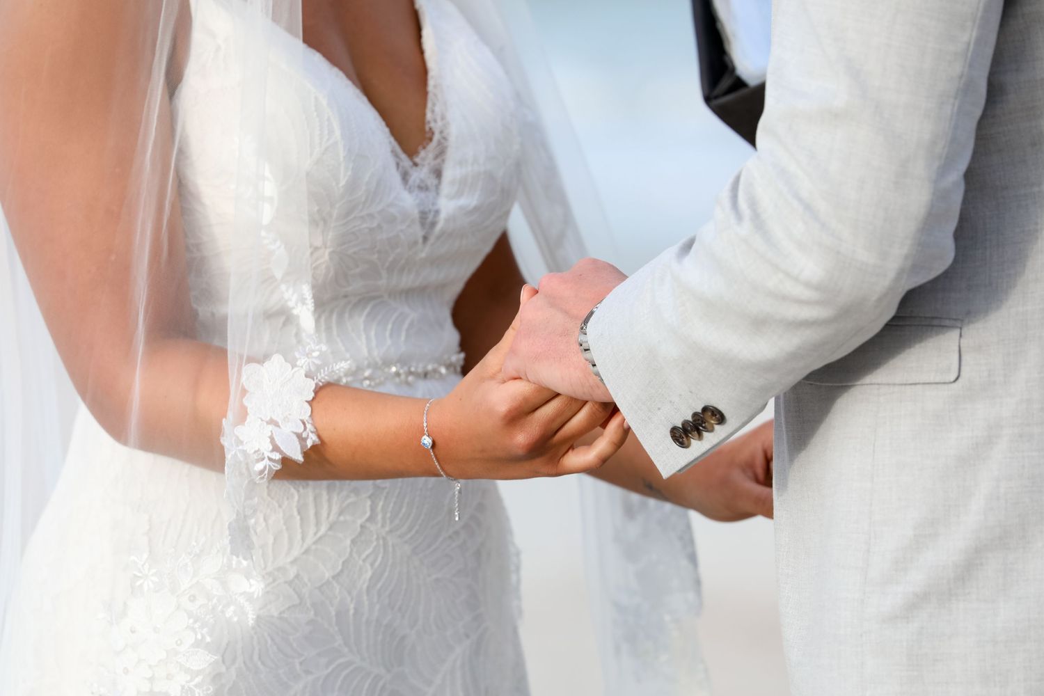Close-up detail of a bride and groom holding hands during their beach wedding ceremony.