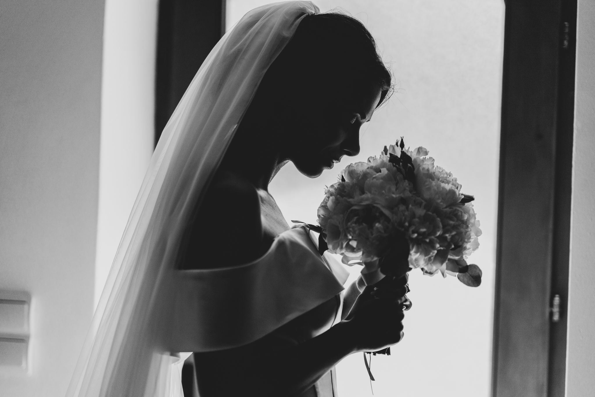 A black and white silhouette photograph of a bride holding her bouquet in a tender moment.