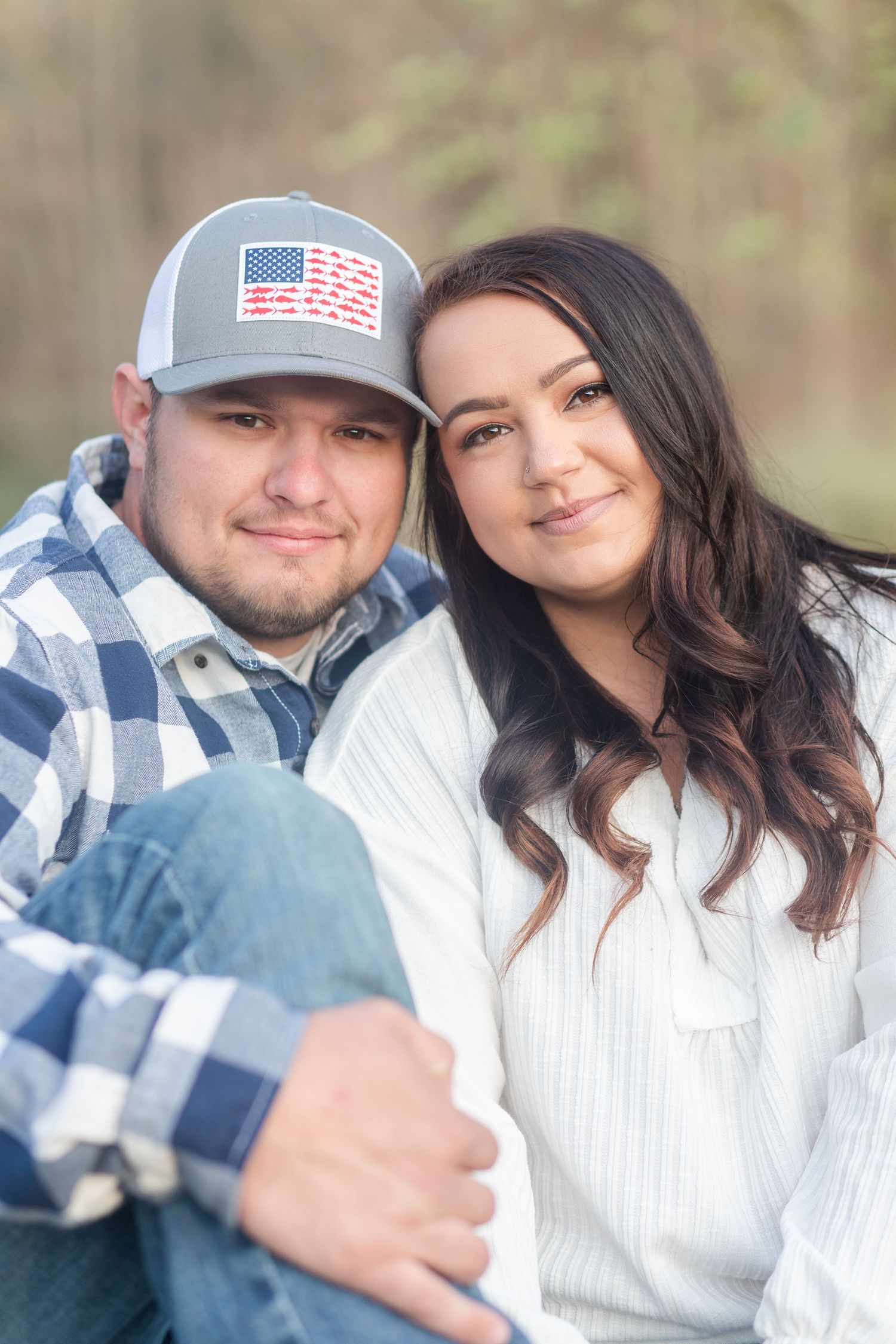 Casual outdoor engagement portrait with couple in plaid and white against natural backdrop.