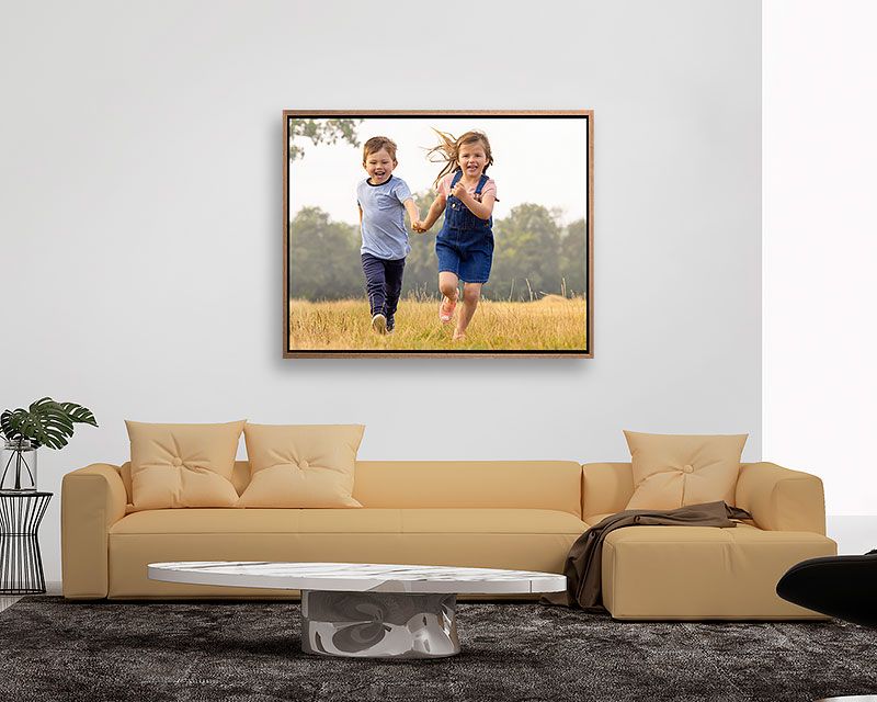 A framed photograph of children running displayed above a modern beige sectional sofa.