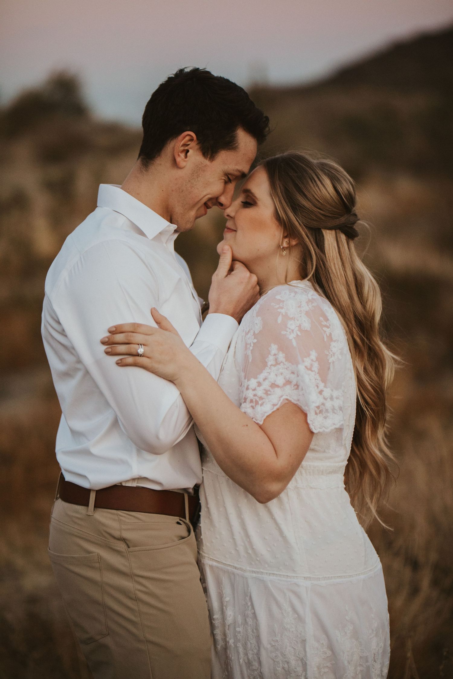 engaged couple holding eachother close and brushing noses with the engagement ring in focus