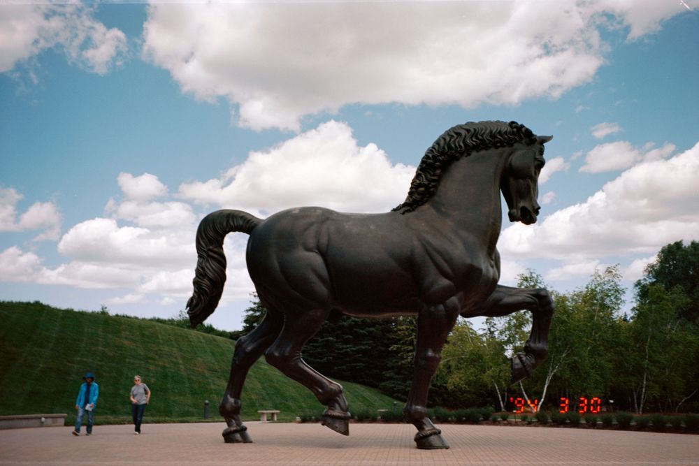 A massive dark bronze horse statue rears dramatically against a summer sky with clouds.