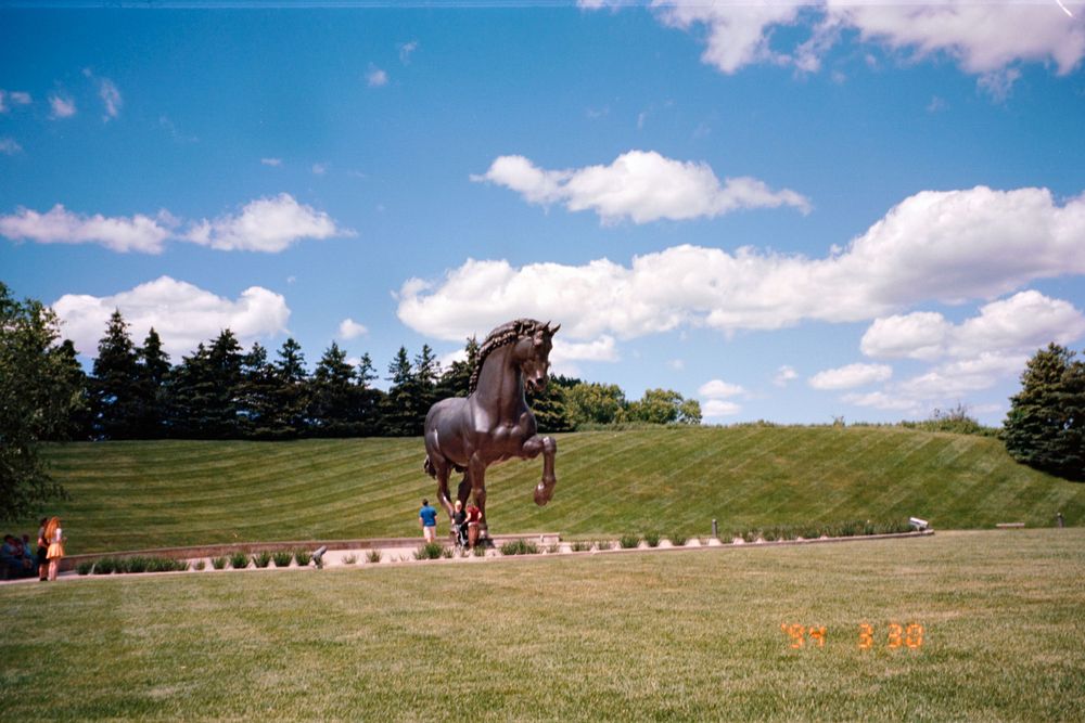 A large bronze horse sculpture stands prominently on a grassy hill against a bright blue sky.