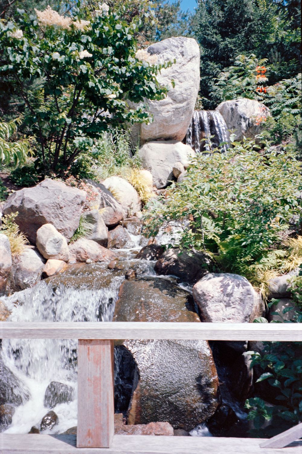 Small waterfall cascading over natural rocks in a landscaped garden setting.