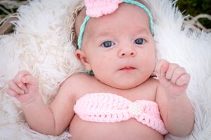 Baby wearing pink headband lies on white furry blanket in pink outfit.