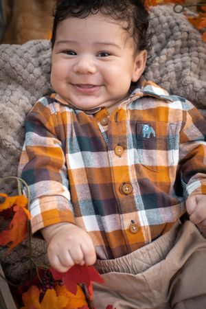 A smiling child wearing a plaid orange and blue flannel shirt rests on a textured gray blanket.