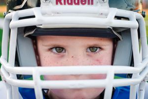 Close-up shot of youth football player wearing white Riddell helmet with face guard.
