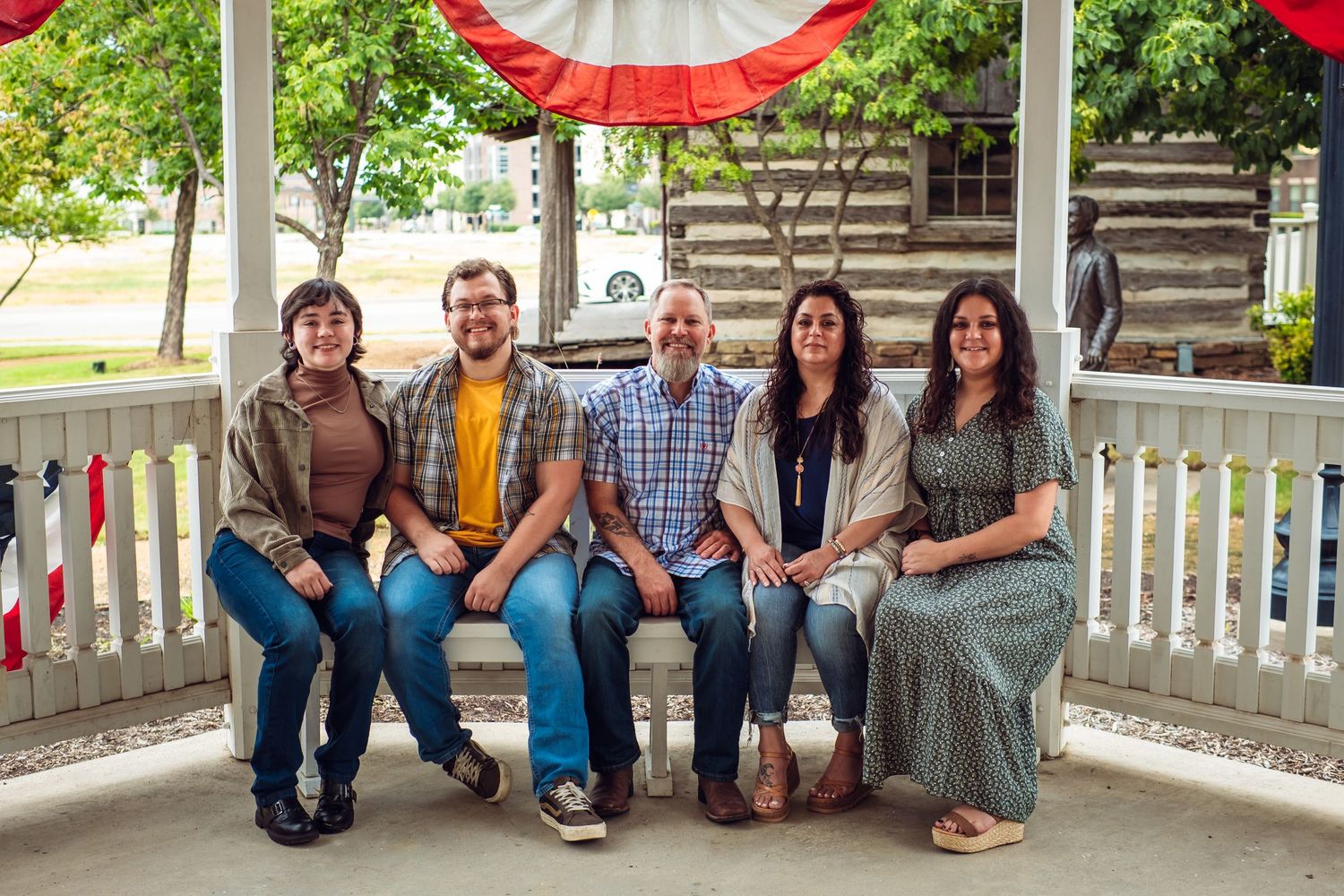 Family group sits casually on white porch with red decorative bunting.
