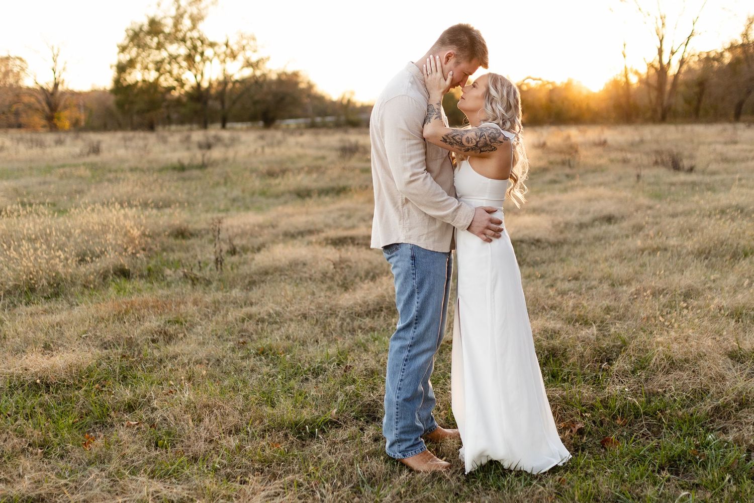 A romantic couple embraces in a golden field during sunset.