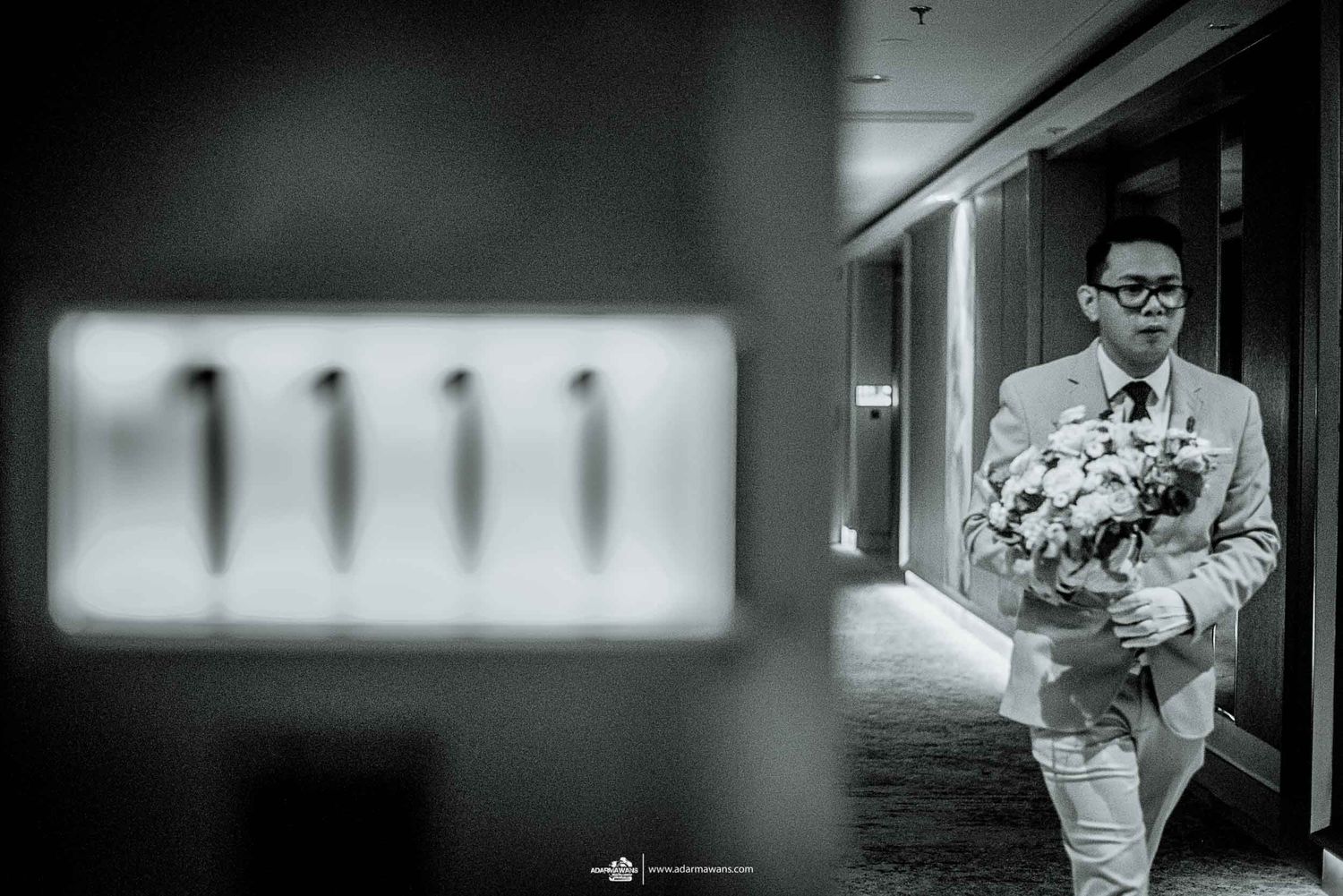 A person in formal attire carries a bouquet of white flowers down a hotel hallway.