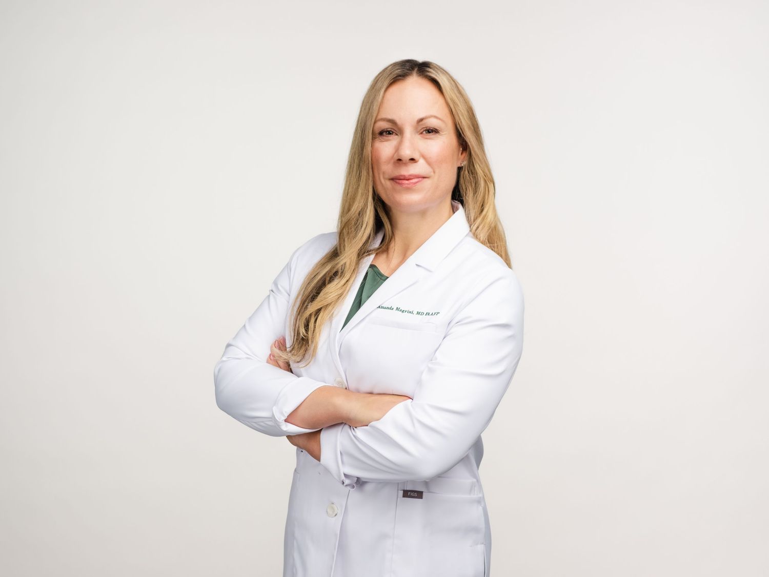 A medical professional in a white lab coat stands confidently with arms crossed against a light background.