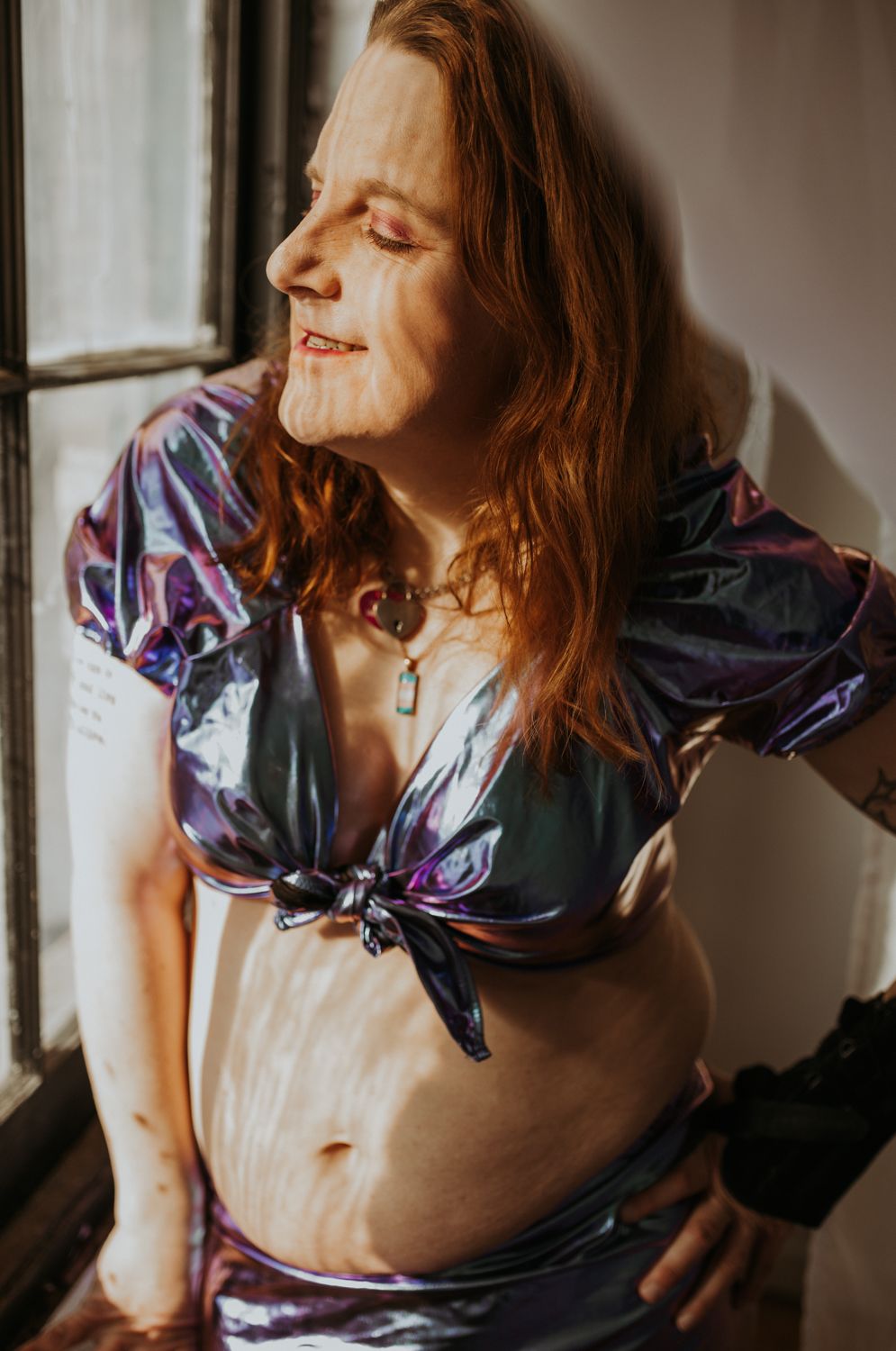 Natural light portrait featuring colorful silk top and expressive pose near window.