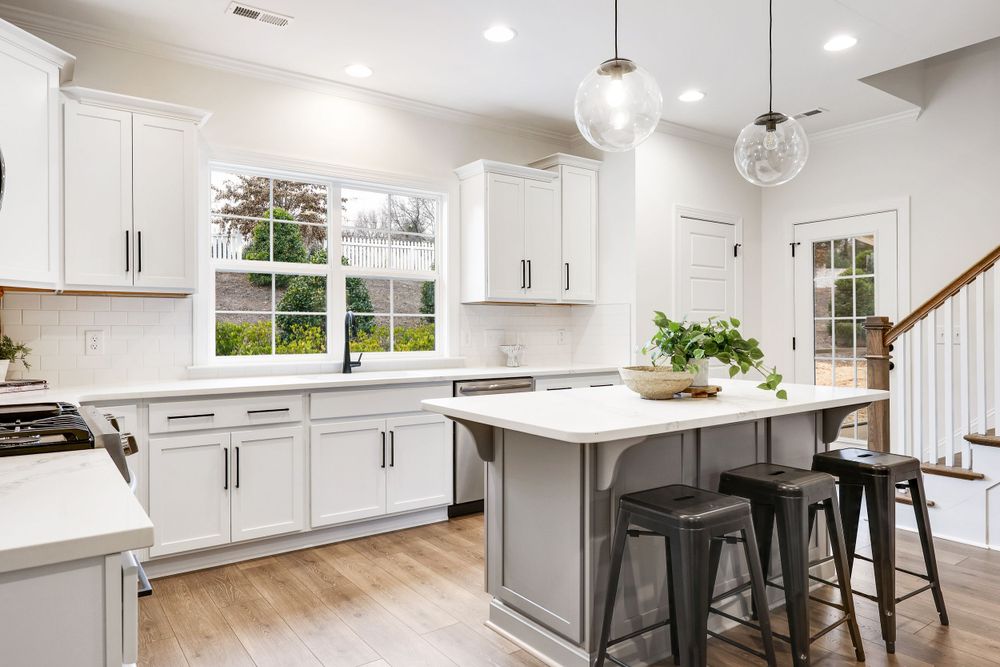 Real estate photo of a bright, modern kitchen in a new home with island and staircase.