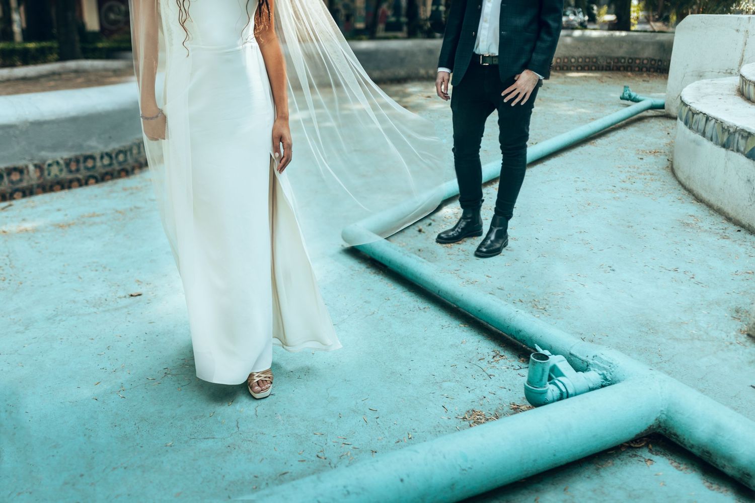 Bride and groom walking together on teal pathway during outdoor wedding celebration.