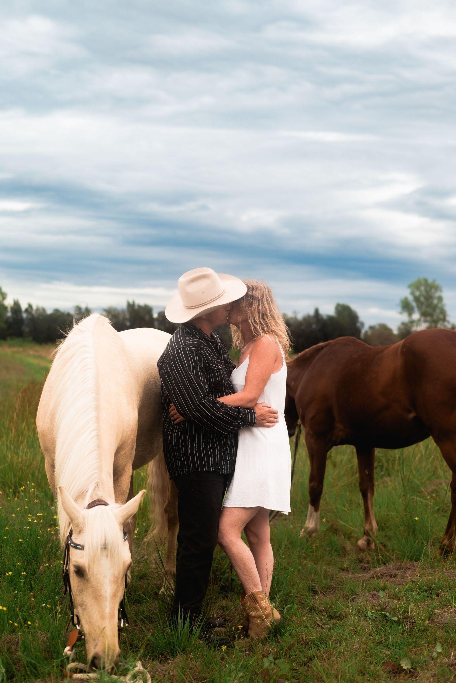 Couple interacting with horses in a grassy field under cloudy skies.