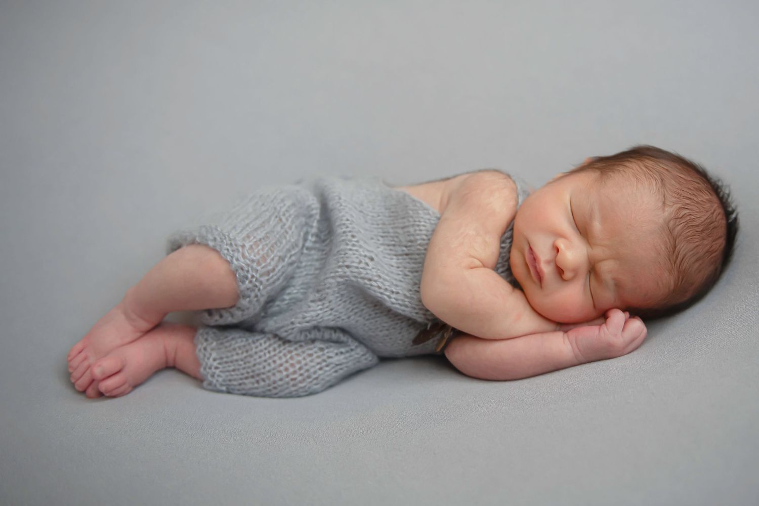 Artistic newborn photography series showing sleeping infant in grey wrap on neutral backdrop.