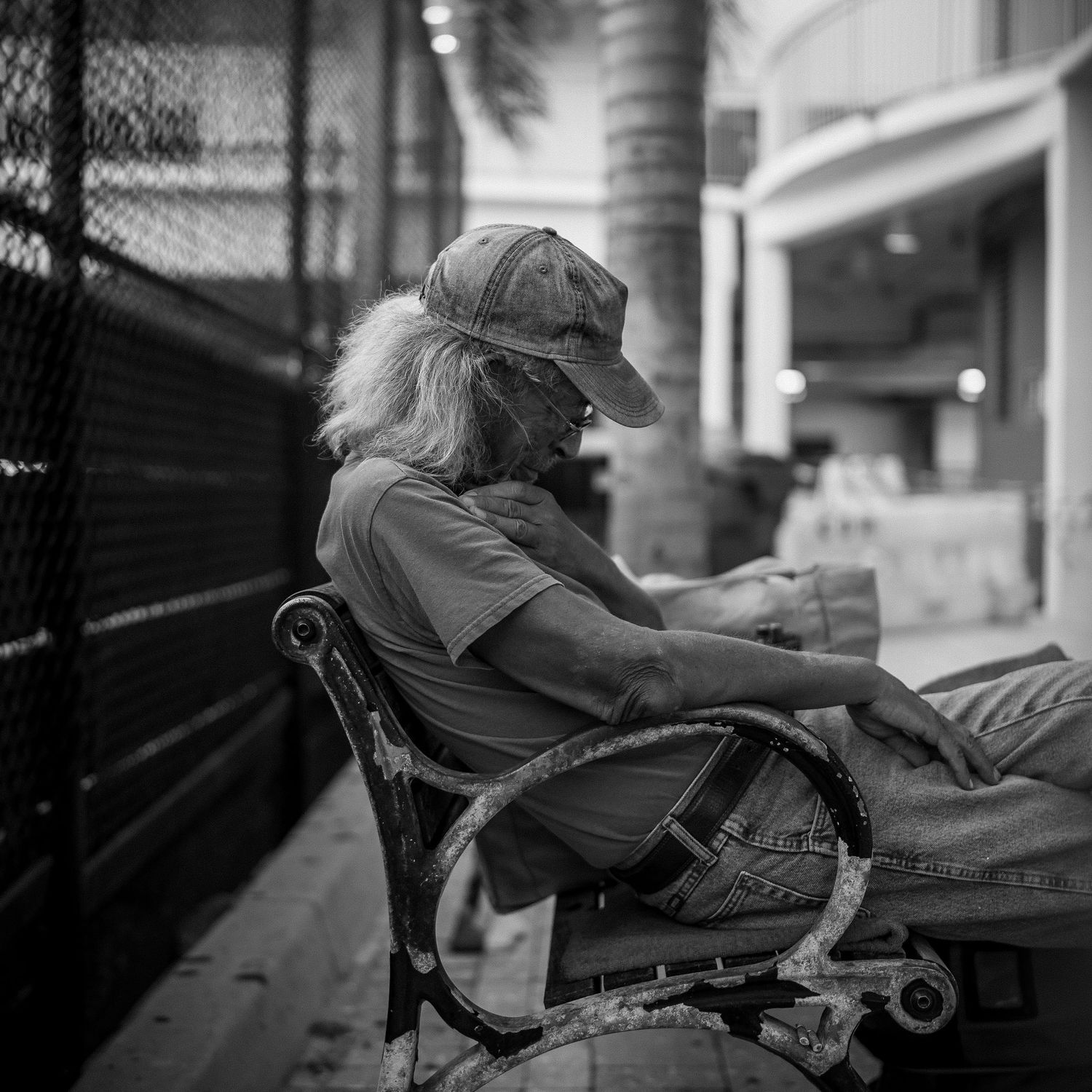 Elderly person resting on park bench in black and white street photography.