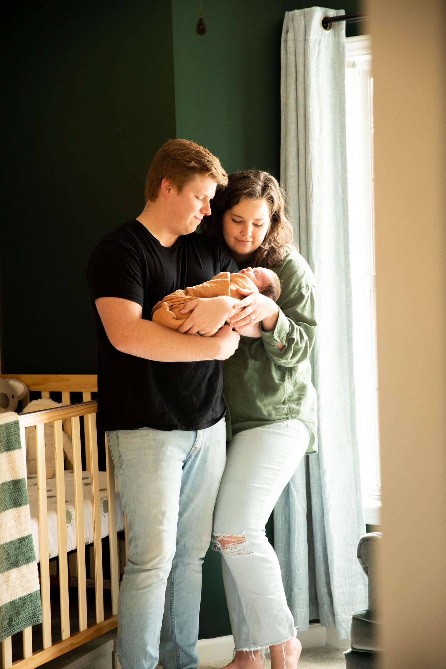 Parents standing by nursery window tenderly holding their newborn baby.