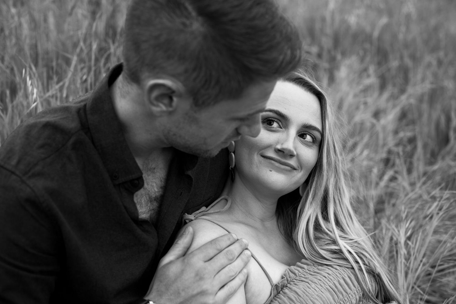 Intimate black and white portrait of a couple sharing a tender moment in tall grass.