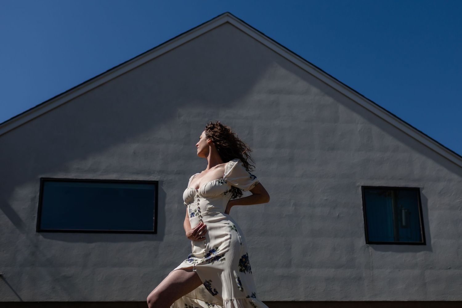 A person in a white dress twirls dramatically against a modern house exterior.