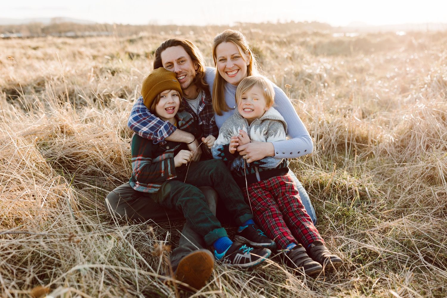 Family sits together in golden field during sunset portrait session.
