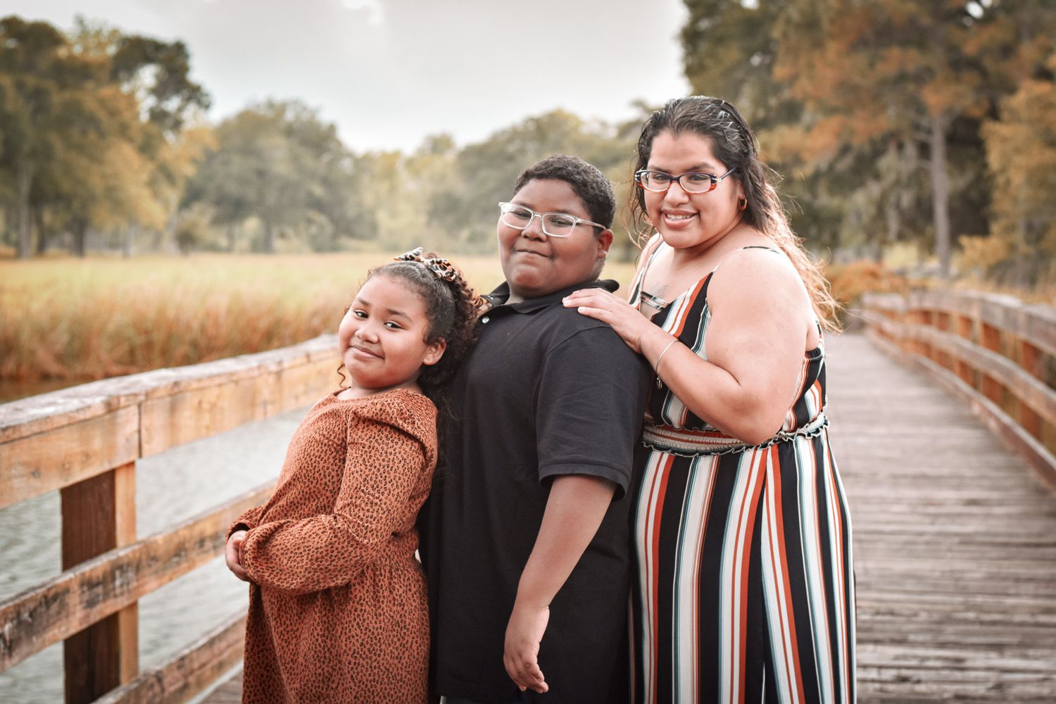 Family portrait of three on a wooden boardwalk during golden hour.