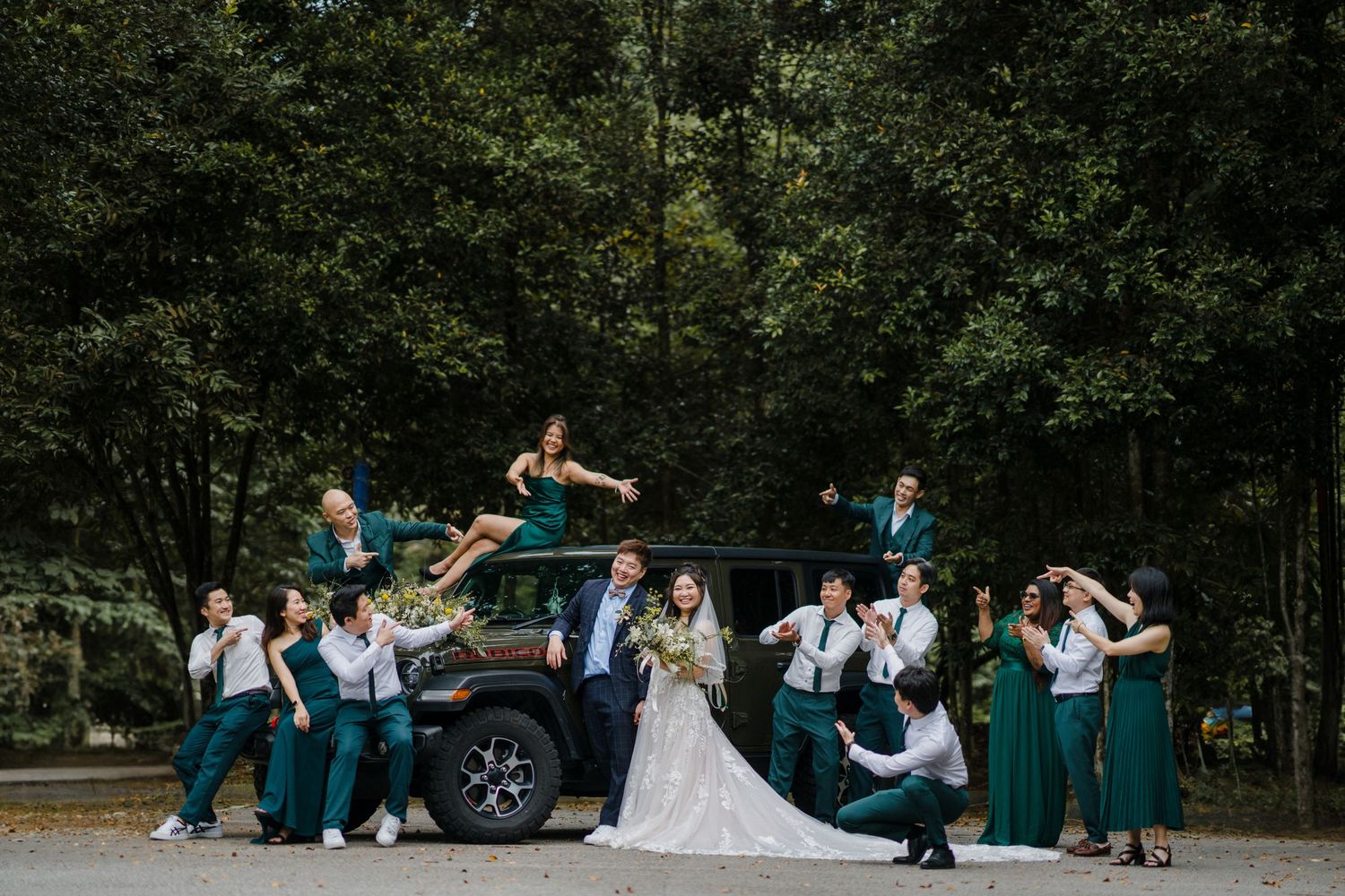 Wedding party in green dresses performs fun group poses outdoors in a park setting.